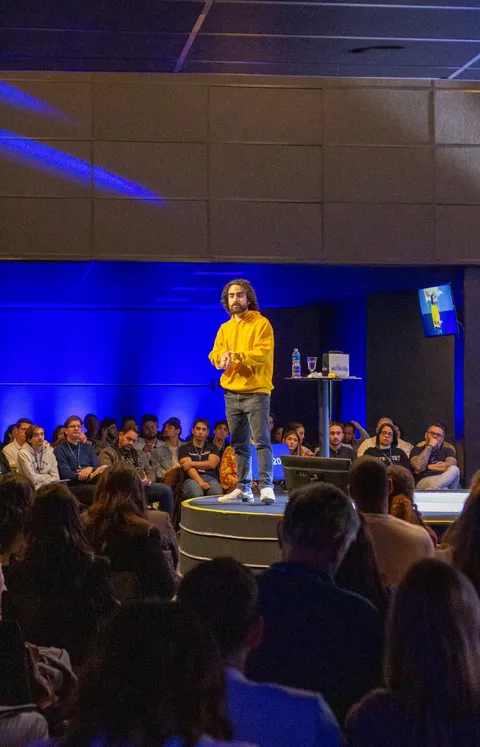 Euriler Jubé em pé no palco falando para uma plateia, com luz azul ao fundo