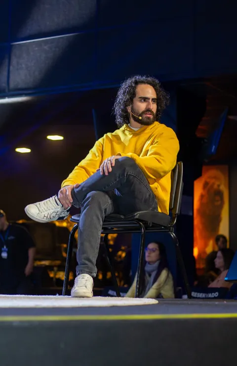 Euriler Jubé sentado numa cadeira no palco, de moletom amarelo